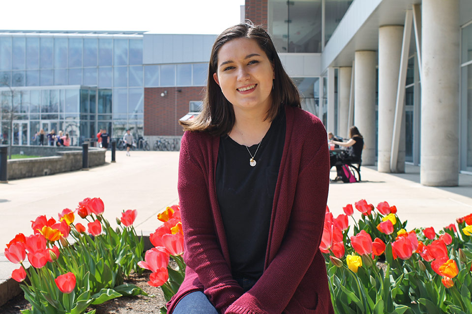 Sarah Emerson sits on a planter filled with tulips outside the Student Fitness Center.